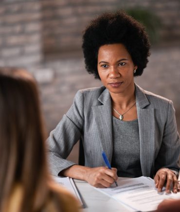 African American bank manager having an interview with her clients and filing paperwork during the meeting.